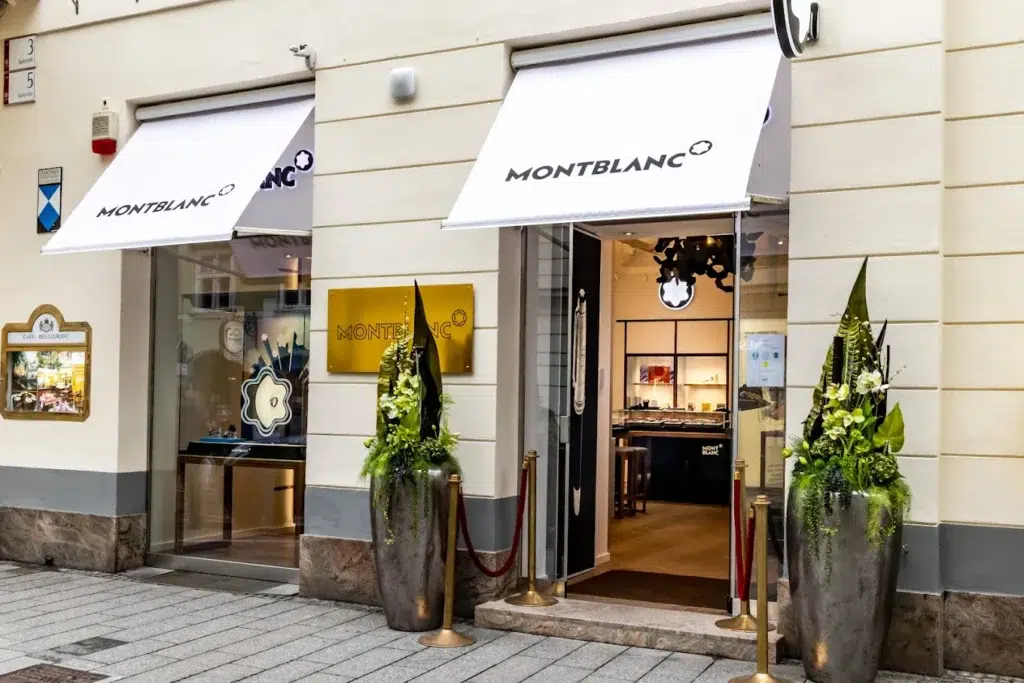 Montblanc-Geschäft; weiße Markisen, zwei große Pflanzgefäße, glatte moderne Fassade.