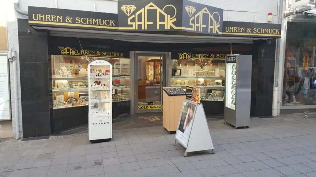 Außenansicht eines Schmuckgeschäfts mit schwarzer Fassade und goldener Schrift, Vitrinen voll Schmuck.