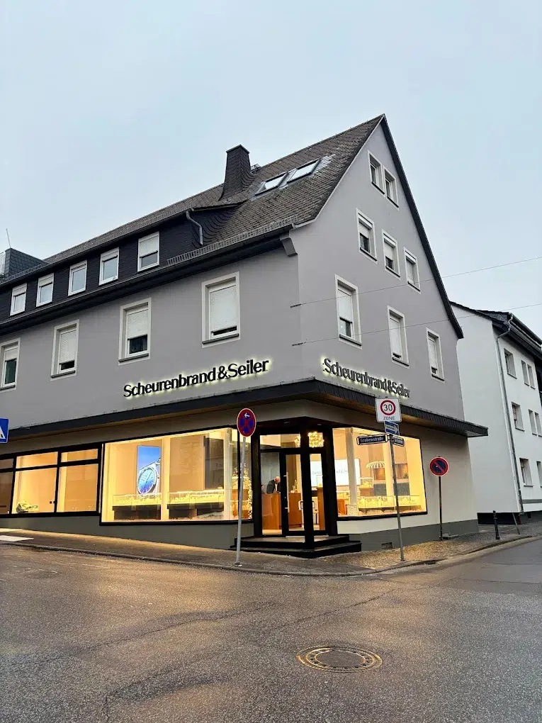 Eckgebäude mit grauer Fassade und großen Schaufenstern unter bewölktem Himmel.
