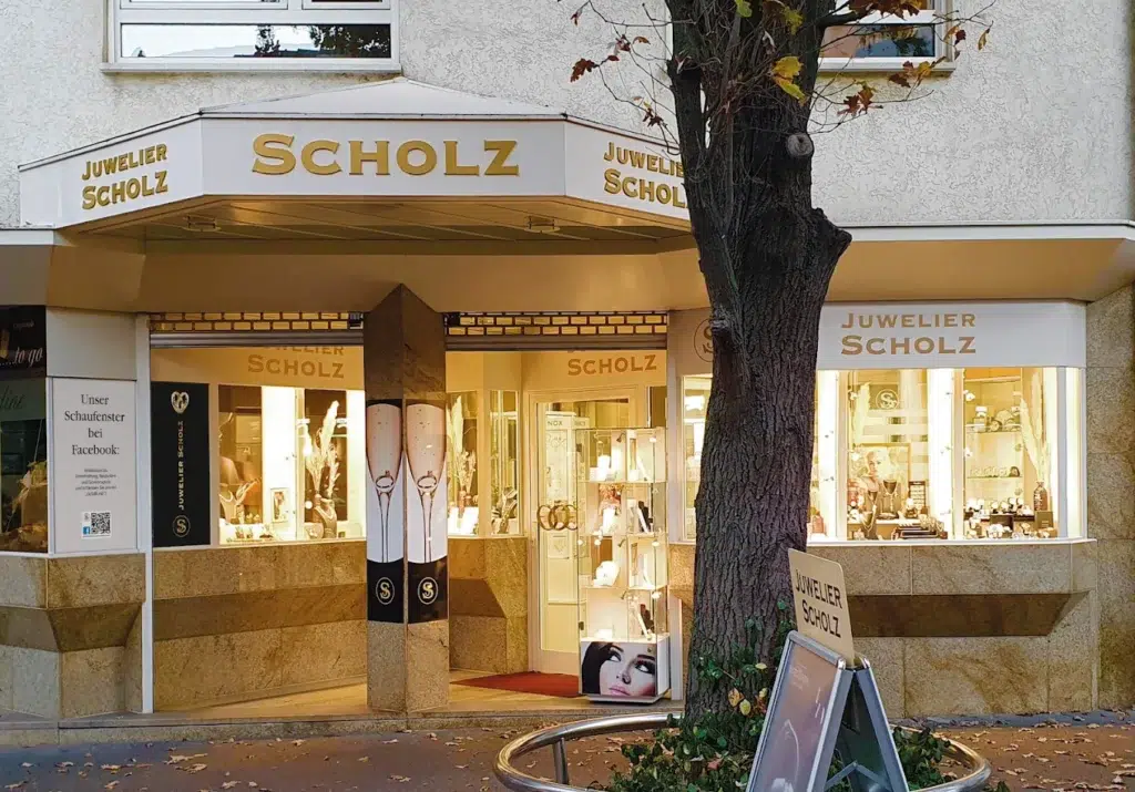 Juwelier Scholz Geschäft, cremefarbenes Äußeres, Herbstbäume, Schaufensterauslagen mit Schmuck.