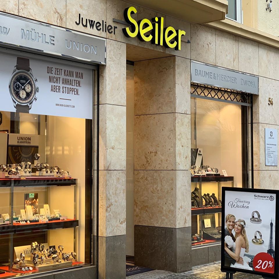 Geschäft "Juwelier Seiler" mit Uhren und Schmuck in der Auslage; Werbeplakate im Fenster.